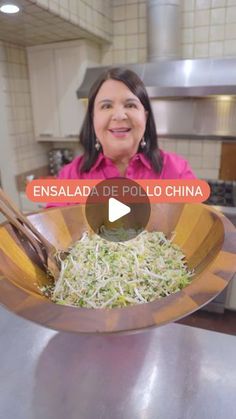 a woman in a pink shirt is holding a wooden bowl with noodles and chopsticks