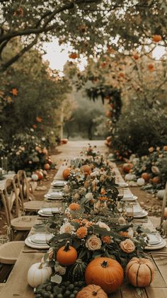 a long table with pumpkins and greenery on it in the middle of an outdoor dining area