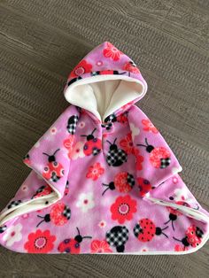 a pink and white dog coat with ladybug print on the hood, sitting on top of a wooden floor