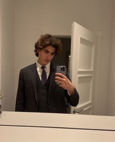 a man in a suit taking a selfie with his cell phone while standing in front of a mirror