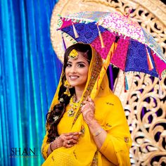 a woman in yellow holding an umbrella and smiling at the camera while standing next to a blue curtain