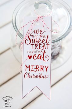 a glass jar filled with christmas treats on top of a white wooden table next to a red string