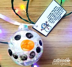 a snowman ornament hanging from a string on a table with christmas lights in the background