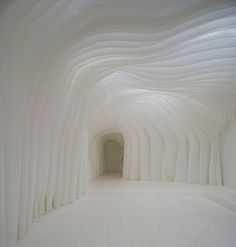 an empty room with white walls and curved columns on the ceiling is lit by sunlight