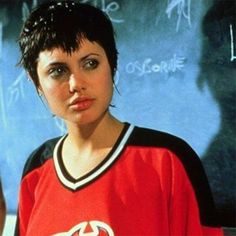 a woman with short black hair wearing a red hockey jersey in front of a chalkboard