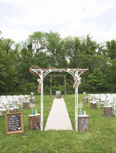 an outdoor ceremony set up with white chairs and chalkboard signs on the grass, surrounded by trees