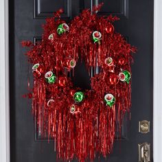 a christmas wreath is hanging on the front door with red tinsel streamers and ornaments