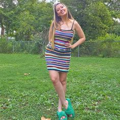 a woman in a multicolored dress is standing on the grass with her hands on her hips