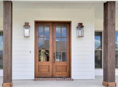 a white house with two wooden doors and some lights on the front porch, along with brick pillars