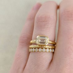 a woman's hand with two gold rings and an emerald ring on top of it