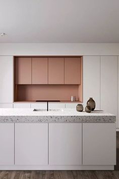 an empty kitchen with white cabinets and marble counter tops, along with two vases on the island