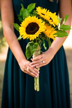 a woman in a green dress holding a bouquet of sunflowers with her hands