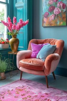 a pink chair sitting in front of a window next to a vase filled with flowers