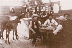 an old photo of men sitting at a table with animals on the wall behind them