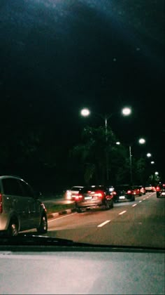 cars are driving down the road at night with street lights in the dark behind them