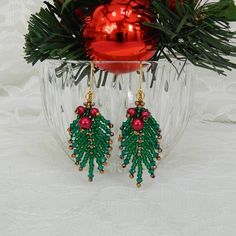 a pair of green and red beaded earrings sitting on top of a glass vase