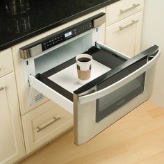 a coffee cup is sitting in the middle of an open microwave drawer that's on top of a counter