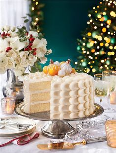 a white cake sitting on top of a table covered in frosting next to a christmas tree