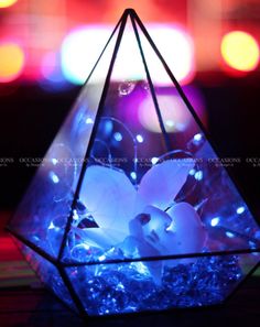 a glass vase filled with flowers on top of a wooden table covered in blue and white lights