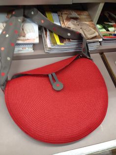 a red purse is sitting on top of a book shelf next to some books and magazines