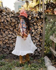 a woman standing next to a pile of firewood wearing a colorful hat and dress