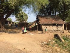 two children are standing in front of a small hut on the side of a dirt road