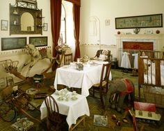 a room filled with lots of tables and chairs covered in white tablecloths next to a fire place