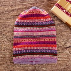 a knitted hat next to a wrapped present on a wooden table with wrapping paper