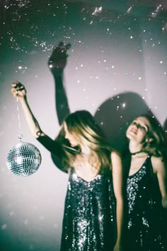 two women in sequin dresses are holding disco balls and looking up at the sky