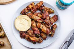 chicken wings with dipping sauce on a white plate next to a cutting board and utensils