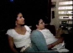 two women sitting next to each other in front of a tv screen with the lights on