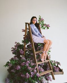 a woman sitting on top of a ladder next to purple flowers