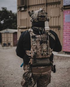 a man in camouflage gear walking down a dirt road with his back to the camera