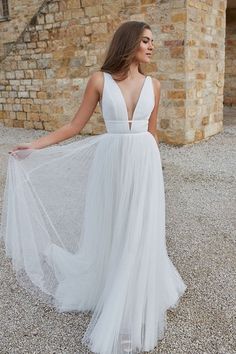 a woman in a white dress standing on gravel with her back turned to the camera