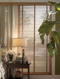 a bedroom with green walls and wooden blinds on the window sill, along with a small table with vases filled with flowers