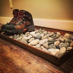 a pair of hiking boots sitting on top of rocks in a wooden tray filled with water