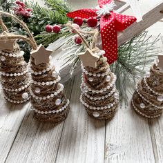 three pine cone christmas trees on a white wooden table with red ribbon and decorations around them