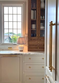 a kitchen with white cabinets and marble counter tops in front of a large open window