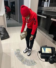 a man in a red hoodie and black pants is looking at money on the floor