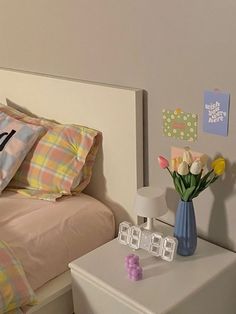 a bed room with a neatly made bed next to a night stand and flower vase