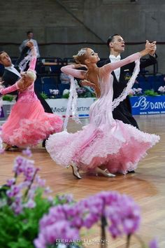 two dancers in pink and white tutus perform on a wooden floor with purple flowers