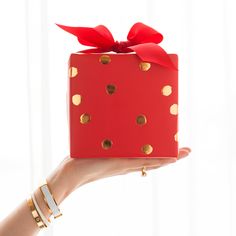 a hand holding a red gift box with gold polka dots and a red ribbon on it