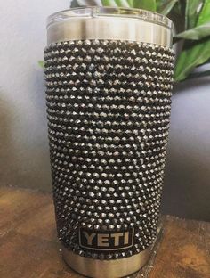 a close up of a metal cup on a table with a plant in the background