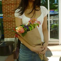 a woman holding a brown paper bag with flowers in it