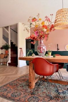 a dining room table with flowers in a vase on top and chairs around the table