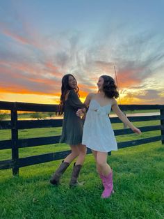 two young women standing next to each other in front of a fence with the sun setting behind them