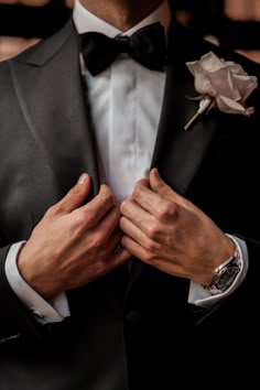 a man in a tuxedo adjusts his bow tie