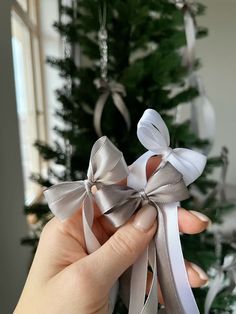 a hand holding a silver bow in front of a christmas tree