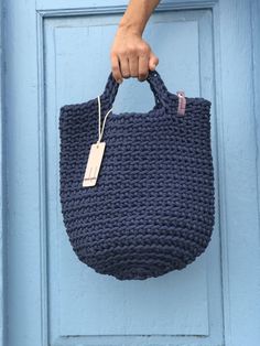 a hand holding a blue crocheted bag with a tag on it's handle