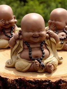 three little buddha statues sitting on top of a tree stump with beads around their necks